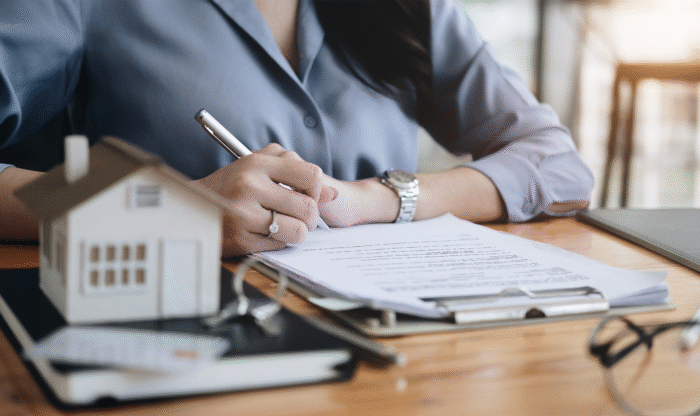 Businesswoman sitting at desk signing papers with house figurine on desk